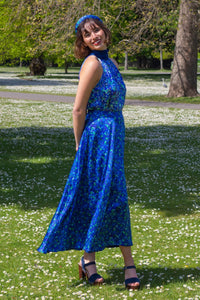 Side view of model wearing reversible voluminous a-line midi silk satin blue floral print skirt, worn with matching halter neck Sophie Top and padded headband.
