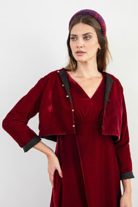 Model wearing reversible box shaped cropped burgundy velvet jacket, with gold bell fastening, worn with matching empire line Amelia dress and Fire Ocean padded headband.