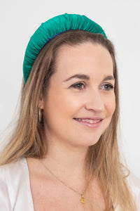 A unique and vibrant emerald green plain silk satin padded headband worn by a model that is stylish and timeless
