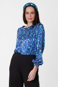 Long sleeve silk satin top with round neck in vibrant green print, worn with Flora Trousers and matching padded headband.