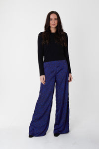 Model wearing reversible high waisted wide palazzo pants in dark blue silk satin print, worn with black high neck jumper.