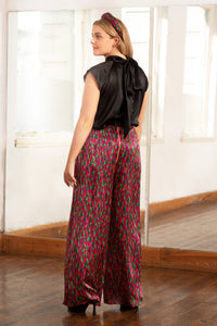 Back view of model wearing an Isabel Manns reversible high waisted silk satin palazzo pants in pink dotted print, worn with halter neck cap sleeved Maya Top in black and padded headband.