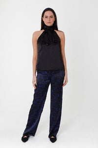Model wearing an Isabel Manns high waisted narrow fit palazzo pants in black camo silk satin print, worn with matching headband and black halter neck Sophie Top.
