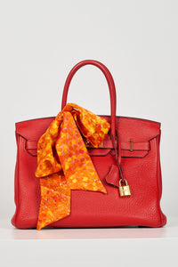a orange printed skinny scarf accessorised on a birkin bag in a bow