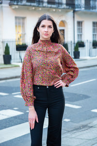 Halter neck silk bamboo top with long raglan sleeves with tie collar in dotted orange/pink print, worn with black jeans.