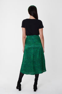 Back view of model wearing vibrant green silk printed Isabel Manns narrow a-line midi skirt with wide waistband, worn with matching padded headband and black t-shirt.