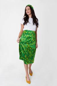 Model wearing a colourful green and yellow silk printed Isabel Manns narrow a-line midi skirt with wide waistband, worn with white t-shirt.