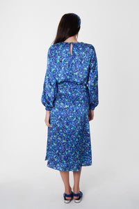 Back view of model wearing blue floral silk printed Isabel Manns narrow a-line midi skirt with wide waistband, worn with matching long sleeve Emily Top and padded headband.