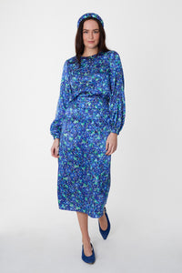 Model wearing blue floral silk printed Isabel Manns narrow a-line midi skirt with wide waistband, worn with matching long sleeve Emily Top and padded headband.