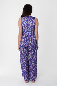 A back view of a sleeveless wide leg silk bamboo jumpsuit and matching belt that comes in a vibrant purple print.