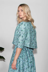 Back view of model wearing reversible box shaped cropped pale green silk satin print jacket, with pearl button, worn with matching Tabitha Dress.