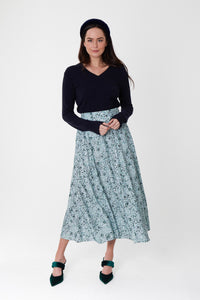 Model wearing a-line midi silk bamboo pale green printed skirt, worn with black v-neck jumper and padded headband.