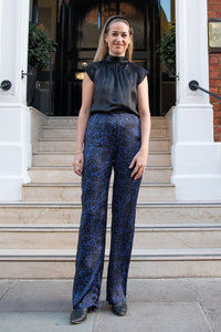 The silk satin floral camo printed trousers with a matching maya black halter neck top with cap sleees in front of a building
