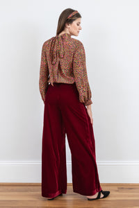 Back view of Model wearing high waisted palazzo pants in burgundy velvet, worn with long sleeved Hannah top in Neon Light and matching headband.