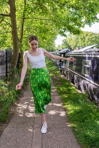 Model wearing wearing a colourful green and yellow silk printed Isabel Manns narrow a-line midi skirt with wide waistband, worn with white vest.