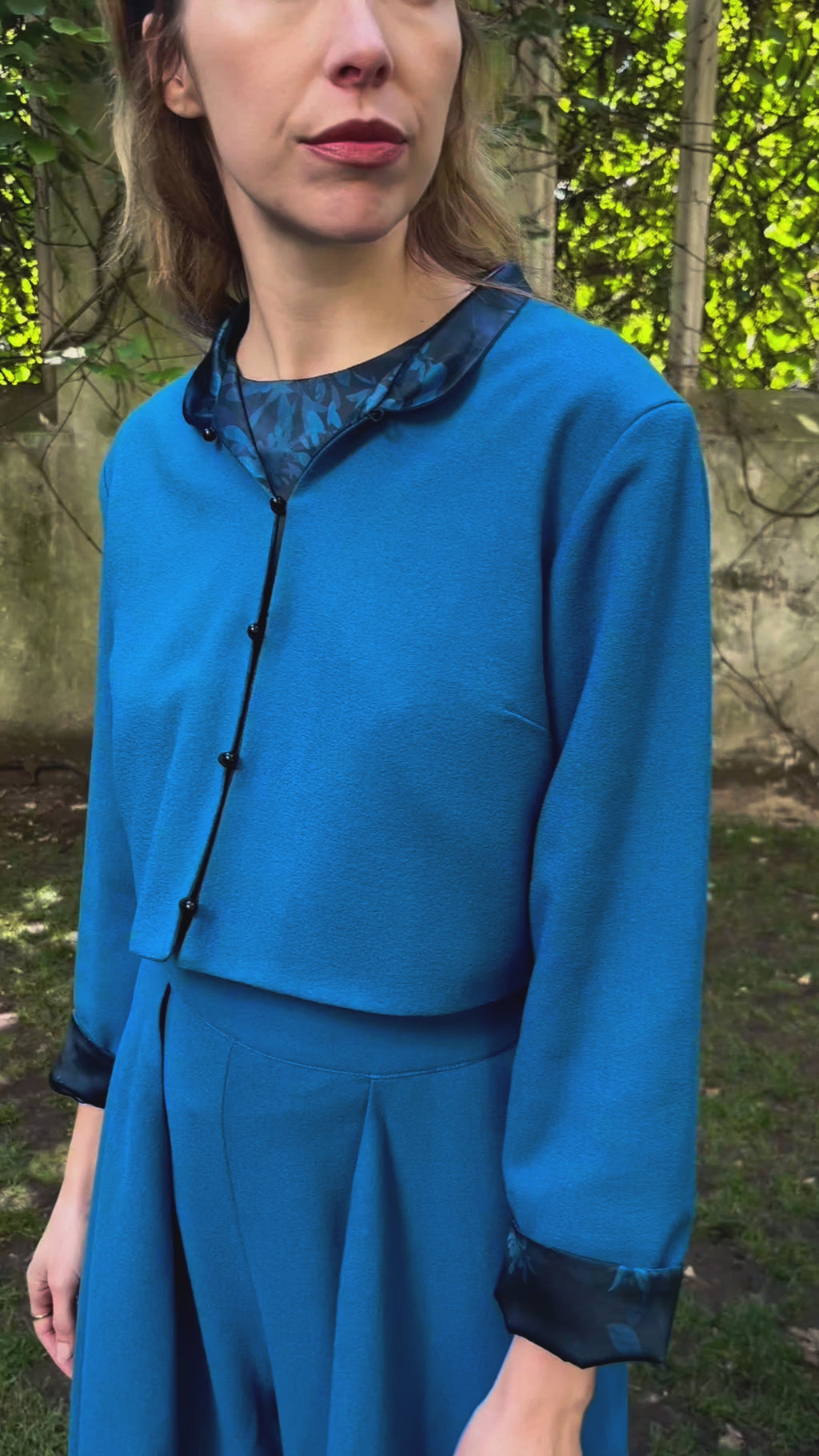 Video of model wearing reversible box shaped cropped teal wool crepe jacket, with mandarin collar and black buttons, worn with matching Penelope Trousers and Emily Top.