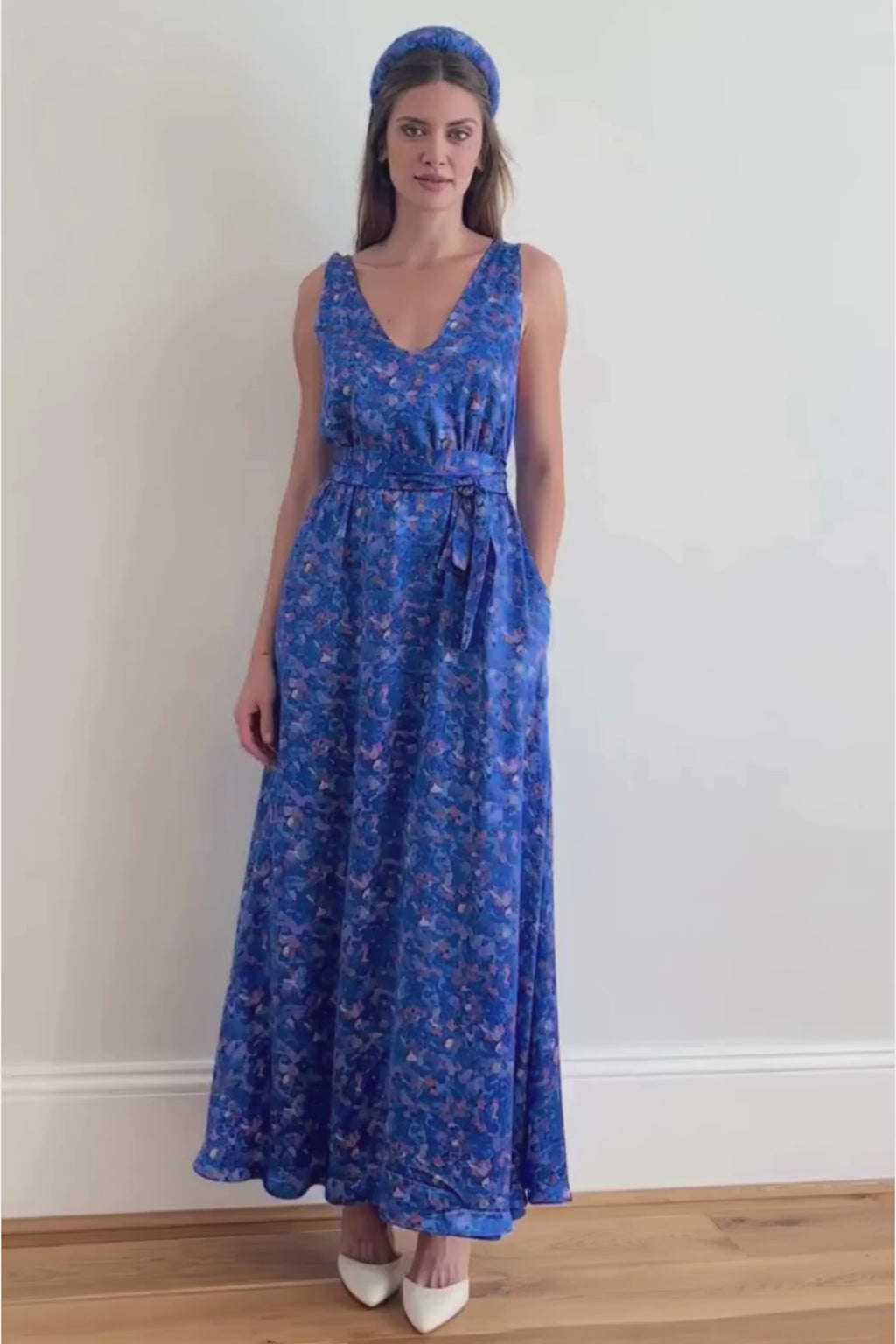 a video showing a model walking into the camera in a long blue printed strappy gown with her hand her in her pocket