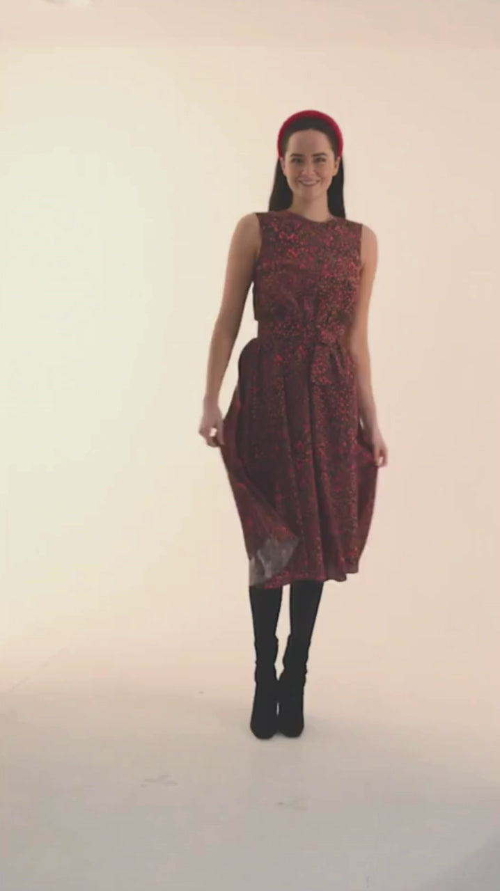 a video showing the twirling and movement of silk crepe de chine featured in a brown and pink printed sleeveless dress worn by a model with a pink headband and black boots