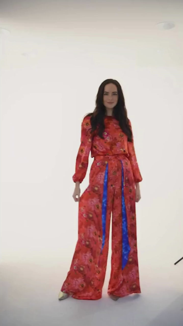 Video of model wearing long sleeve silk satin top with low back in coral floral print and matching Penelope Trousers.