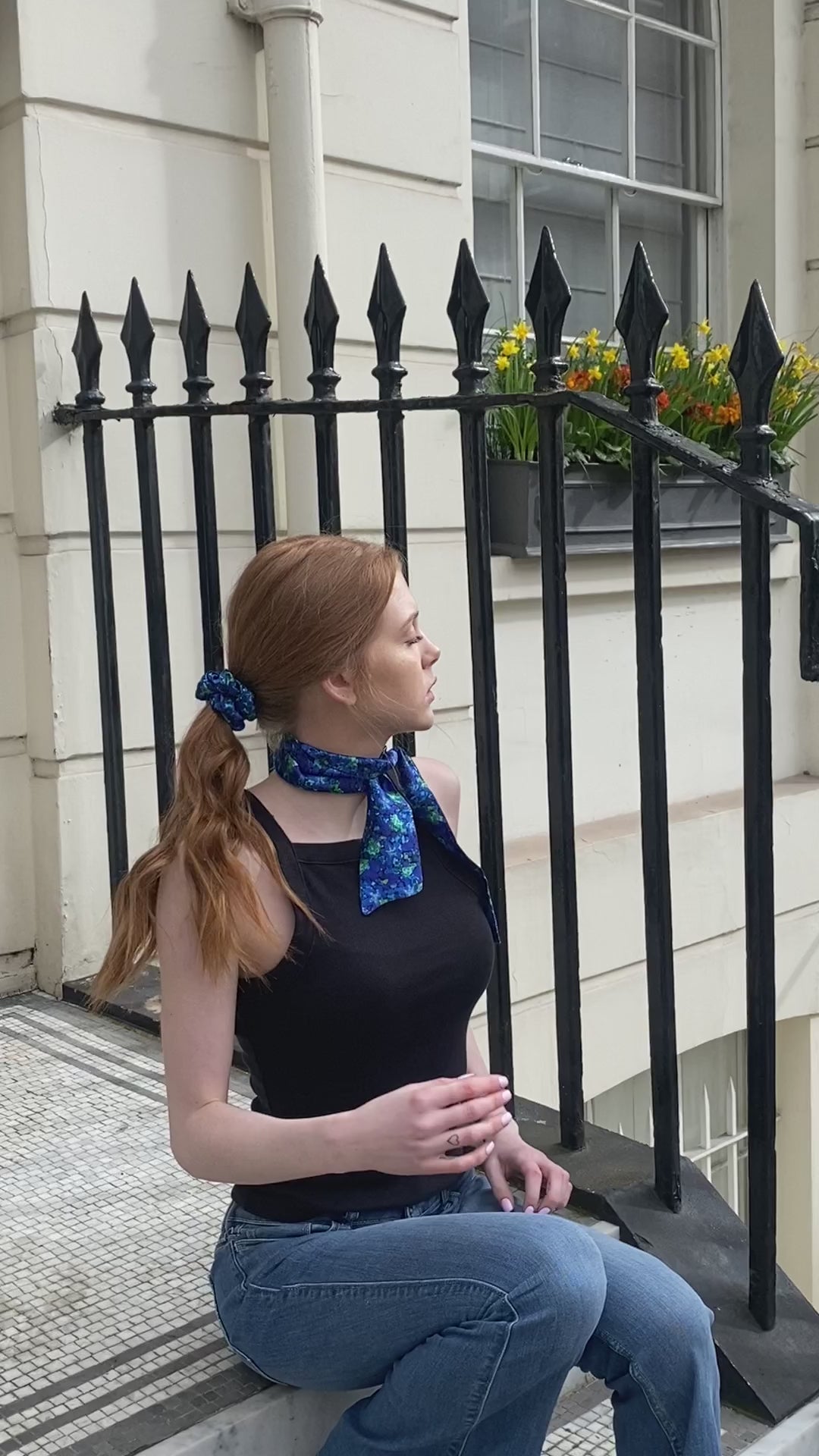 Video of Narrow silk satin scarf in blue floral print, with matching scrunchie, black vest and jeans.