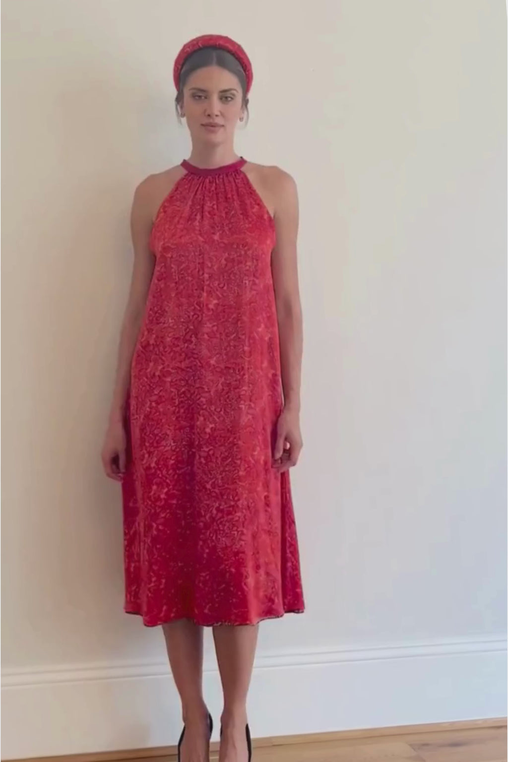 a video showing a women walking in a midi length halter neck silk satin dress in a vibrant red print