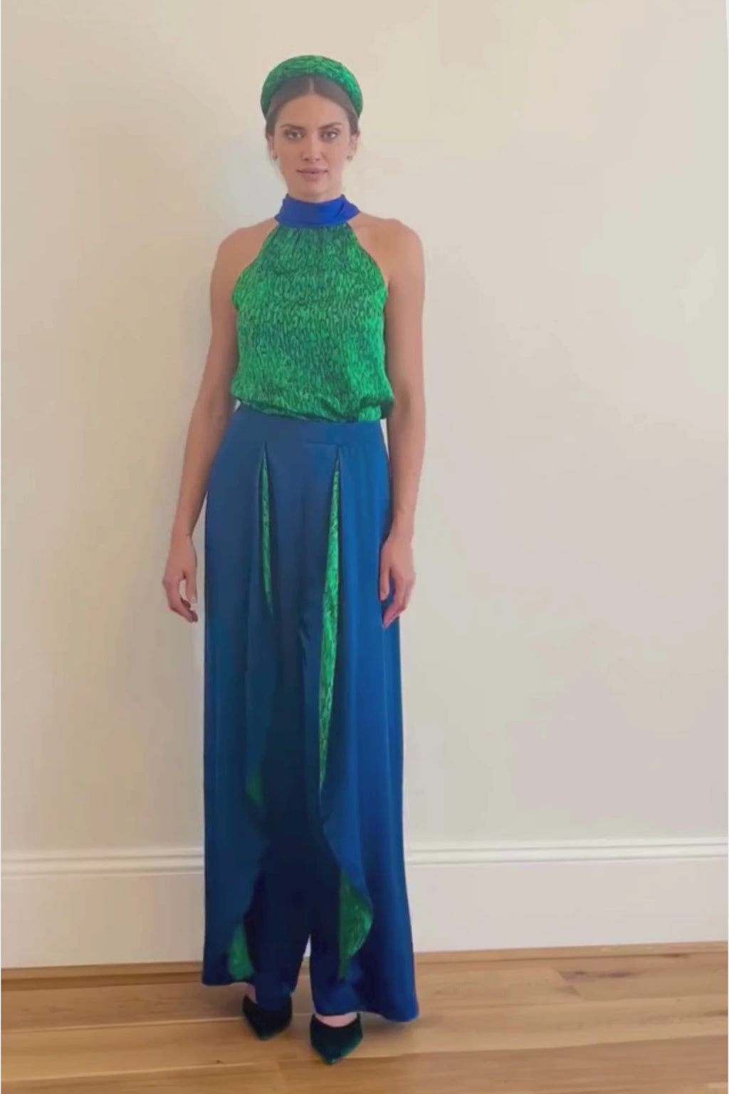 Video of model wearing an Isabel Manns wide leg wrap around style silk viscose trousers in navy and contrasting vibrant green print lining, worn with matching halterneck Sophie Top in vibrant green print and padded headband.