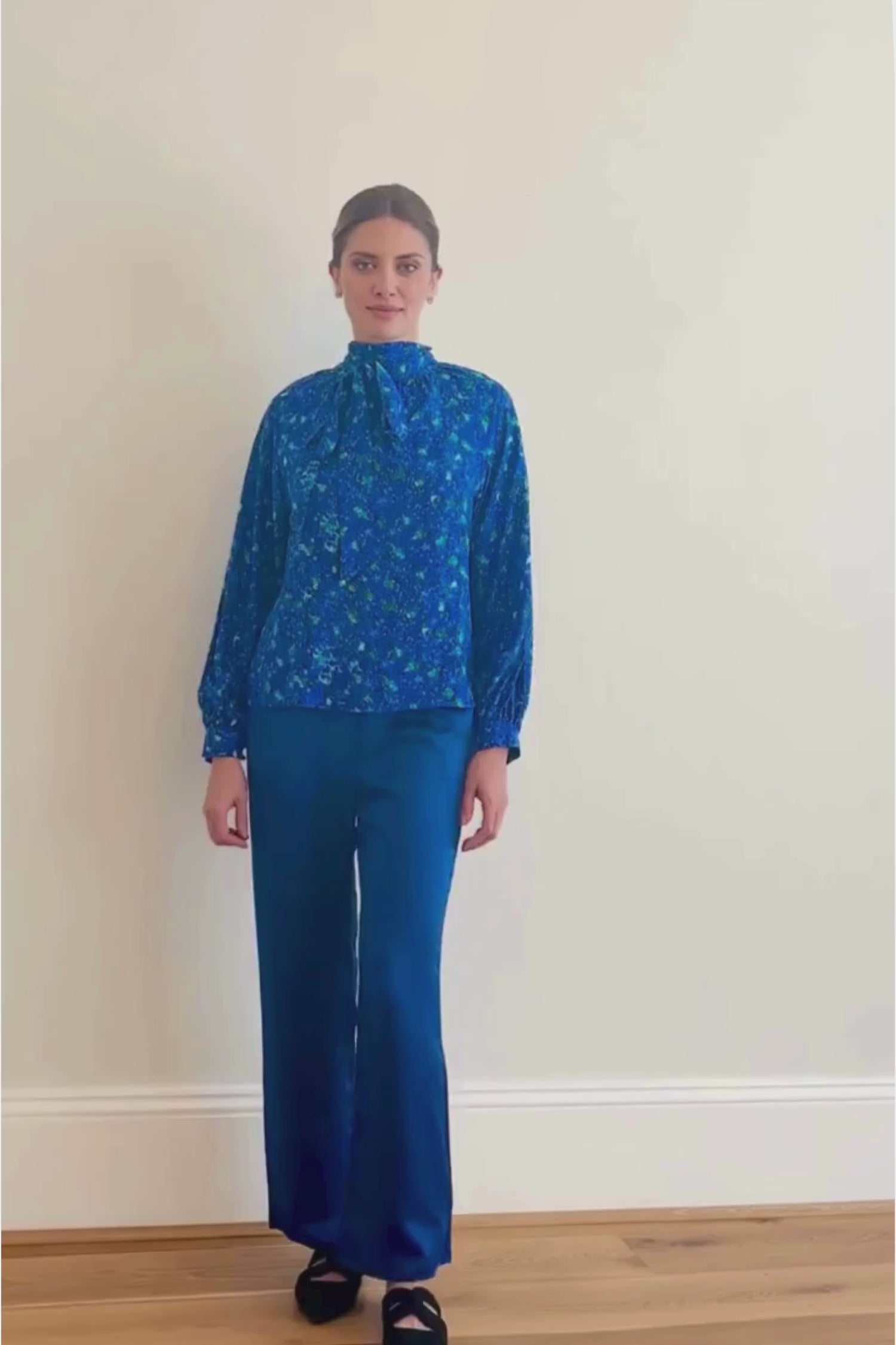 Video of model wearing An Isabel Manns halter neck silk bamboo top with long raglan sleeves with tie collar in blue floral print and Georgia Trousers navy.
