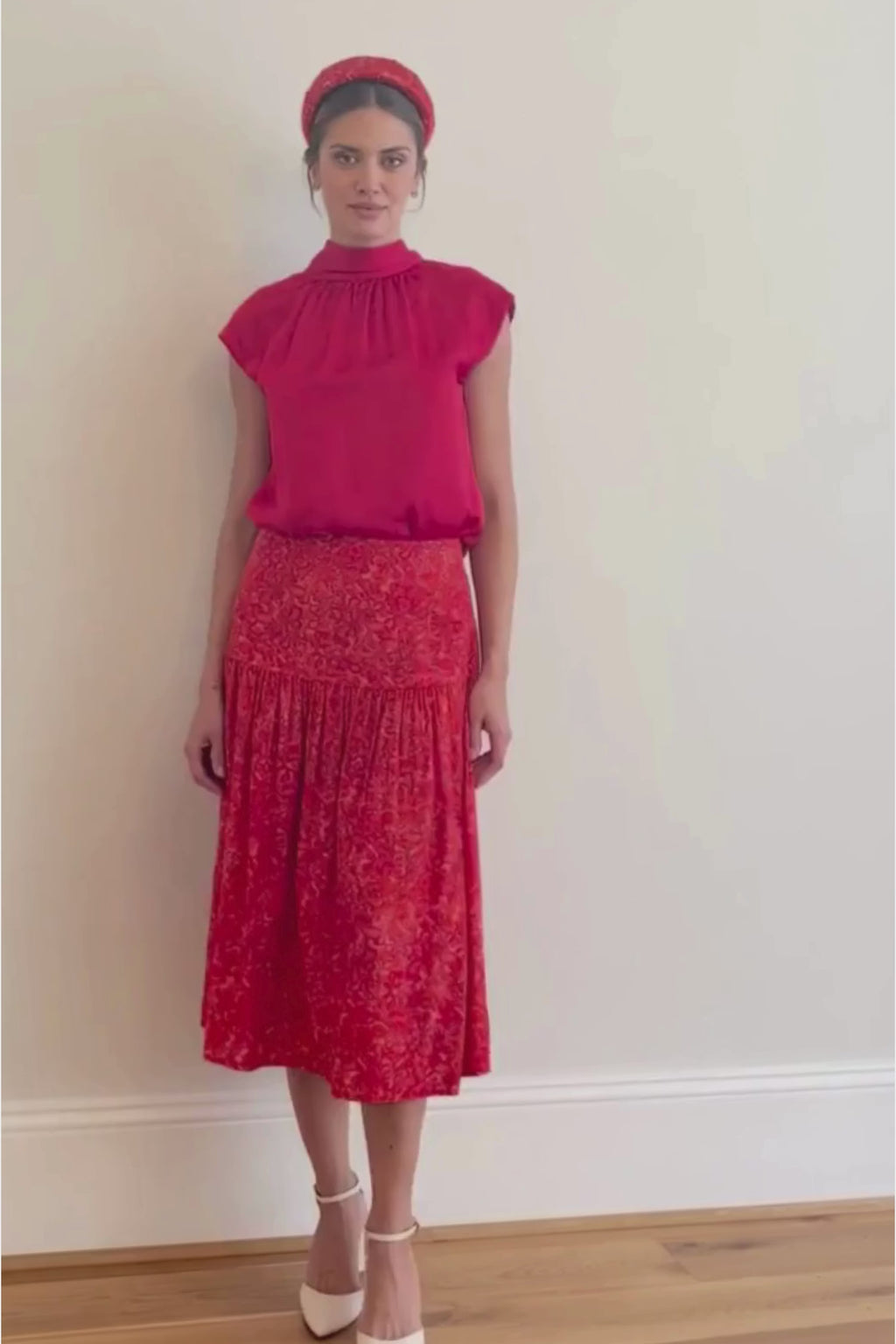 Video of model wearing a-line midi silk bamboo skirt with an extra wide waistband and gathered detail from hips down in vibrant red swirl print, worn with matching padded headband and halter neck cap sleeve Maya top in Raspberry Pink.