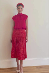 Video of model wearing a-line midi silk bamboo skirt with an extra wide waistband and gathered detail from hips down in vibrant red swirl print, worn with matching padded headband and halter neck cap sleeve Maya top in Raspberry Pink.