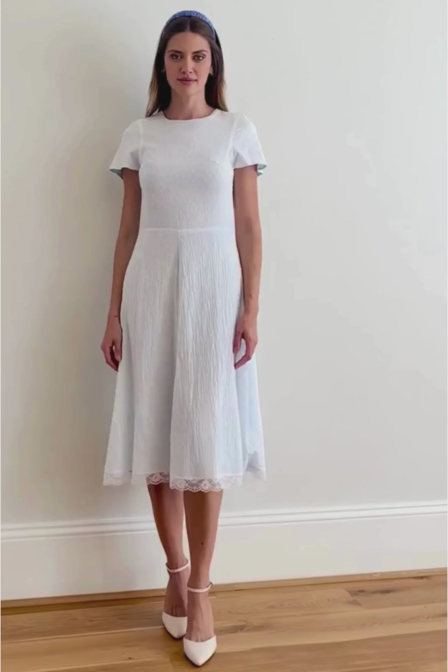 a model walking in a video to show the stunning white cotton midi dress with white lace trim detail at the hem