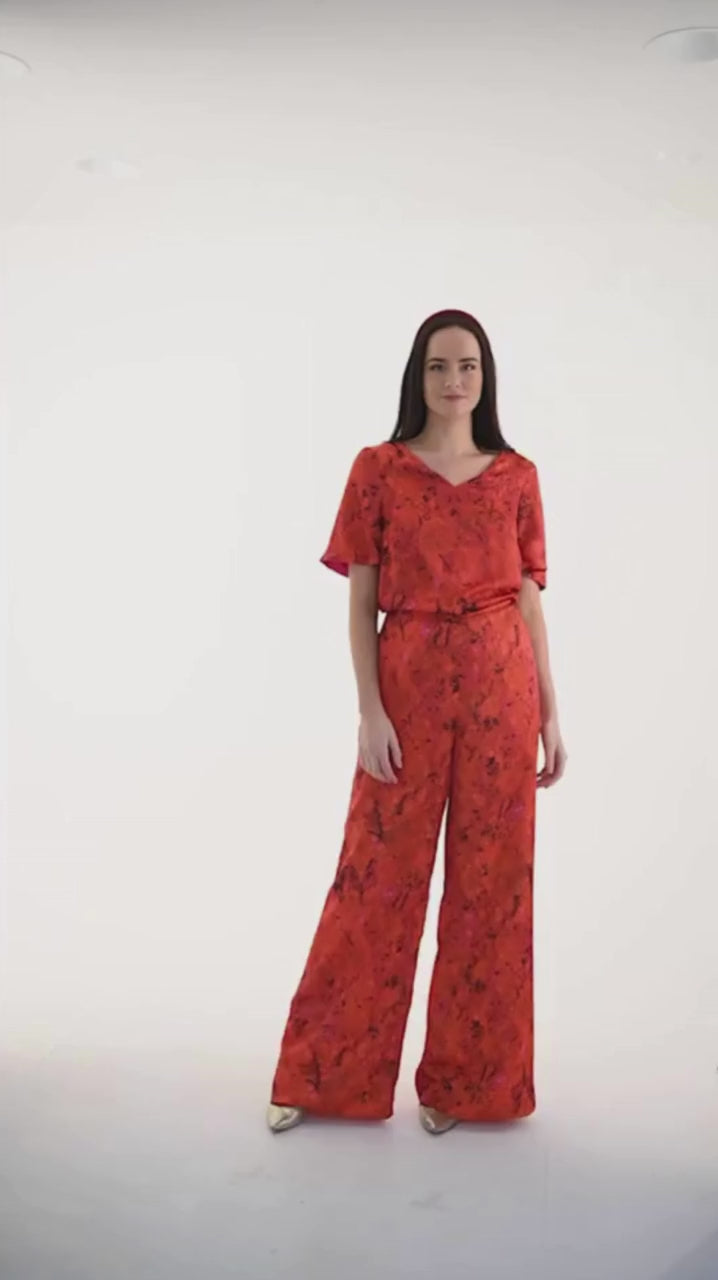 Video of Model wearing an Isabel Manns reversible high waisted silk satin palazzo pants in orange/red floral print, worn with matching v-neck with elbow length sleeves Eleanor Top and burgundy velvet headband.