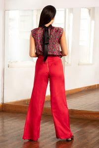 Back view of model wearing an Isabel Manns reversible high waisted silk satin palazzo pants in Raspberry Pink, worn with matching halter neck cap sleeved Maya Top in black and padded headband.