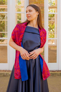 a reversible silk satin scarf in a red pebble print and cobalt reverse side worn effortlessly on a model who is wearing a gown.