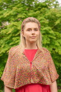 Model wearing reversible orange/pink dotted print silk satin shawl with pearl fastener at the chest, with matching padded headband and raspberry pink Victoria Gown.