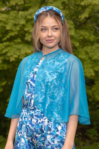 Side view of Model wearing curved elbow length turquoise chiffon shawl with pearl fastener, worn with Penny Jumpsuit Serenity blue and matching padded headband.