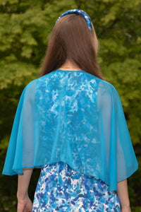 Back view of Model wearing curved elbow length turquoise chiffon shawl with pearl fastener, worn with Penny Jumpsuit Serenity blue and matching padded headband.