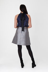 a silver jacquard short skirt with black tights and boots styled with a silk halter neck top back view