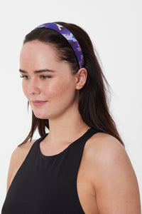 a silk headband comprising of a patchwork print made of purple shades worn by a model